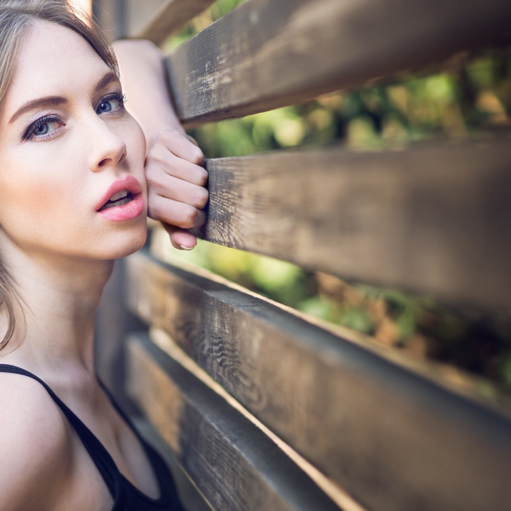 Красивая голубоглазая девушка у деревянного забора 