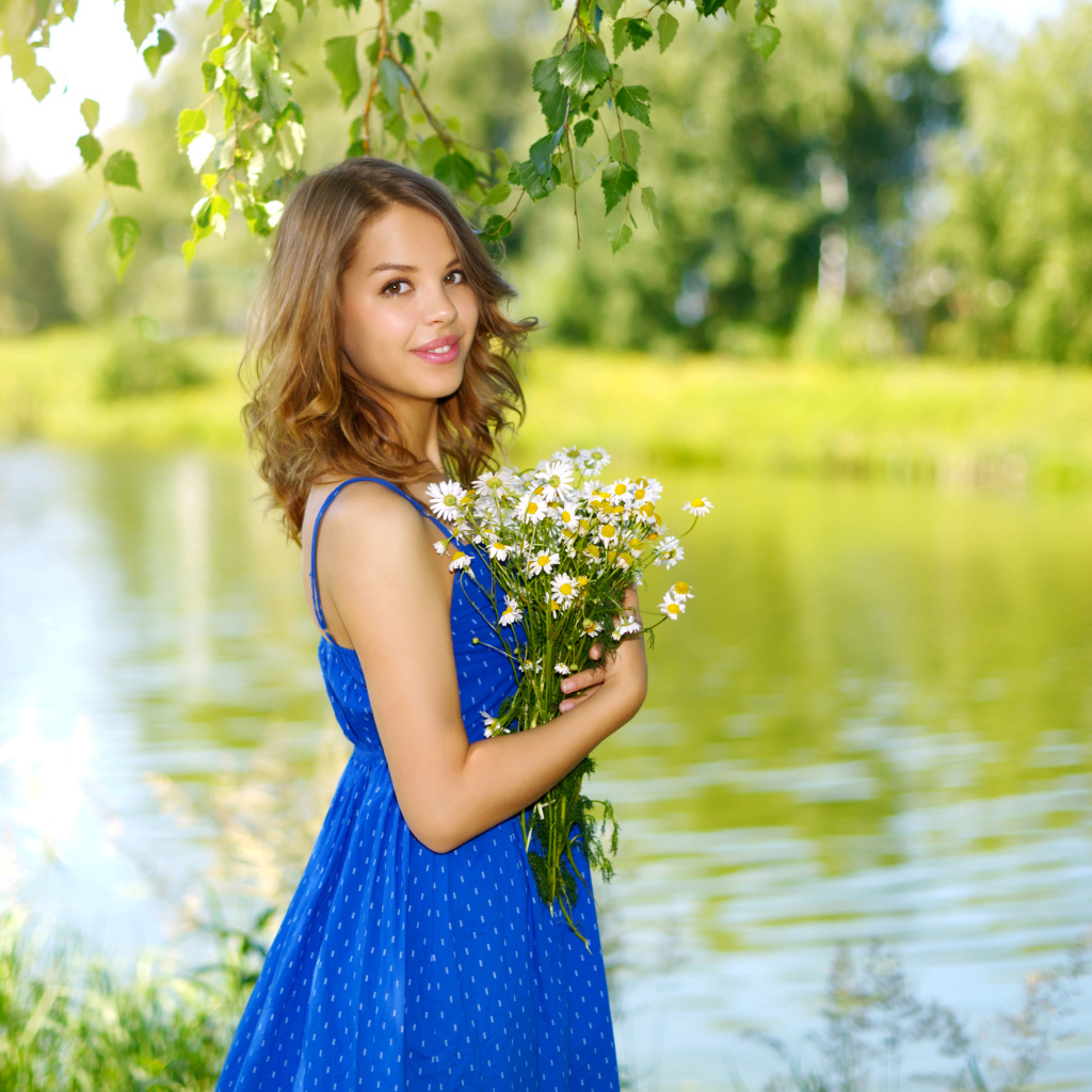Красивая девушка шатенка в синем сарафане с букетом ромашек у воды
