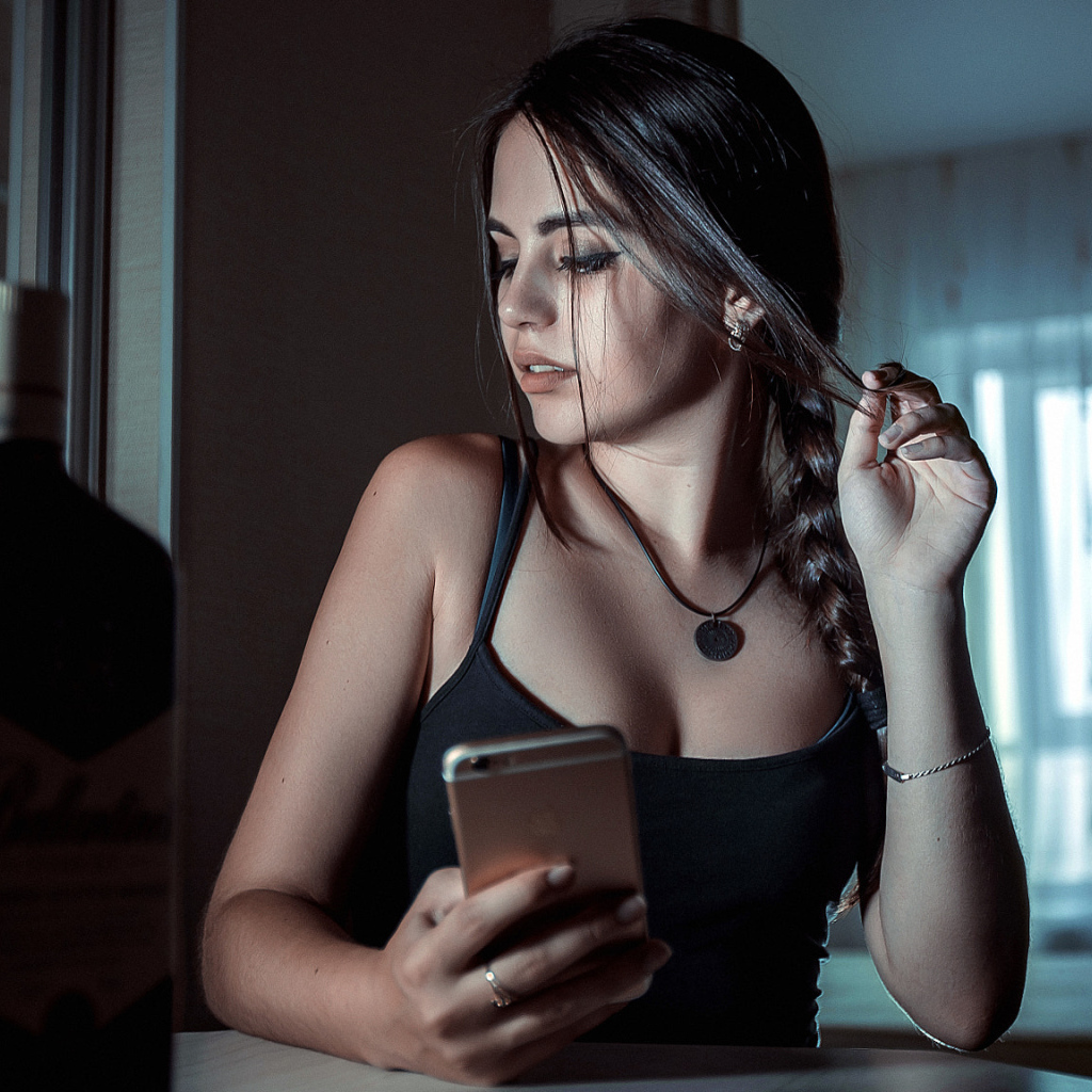 Красивая брюнетка с телефоном в руках и бутылкой