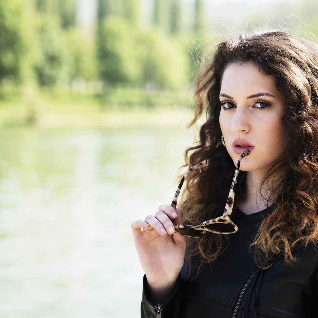 Красивая девушка с волнистыми волосами с очками в руках 