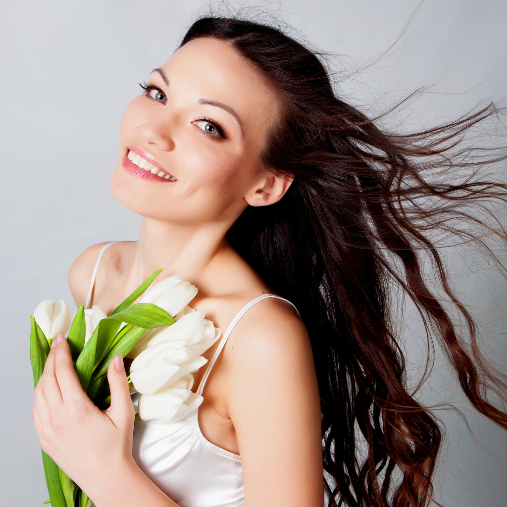 Красивая улыбающаяся брюнетка с букетом тюльпанов на сером фоне