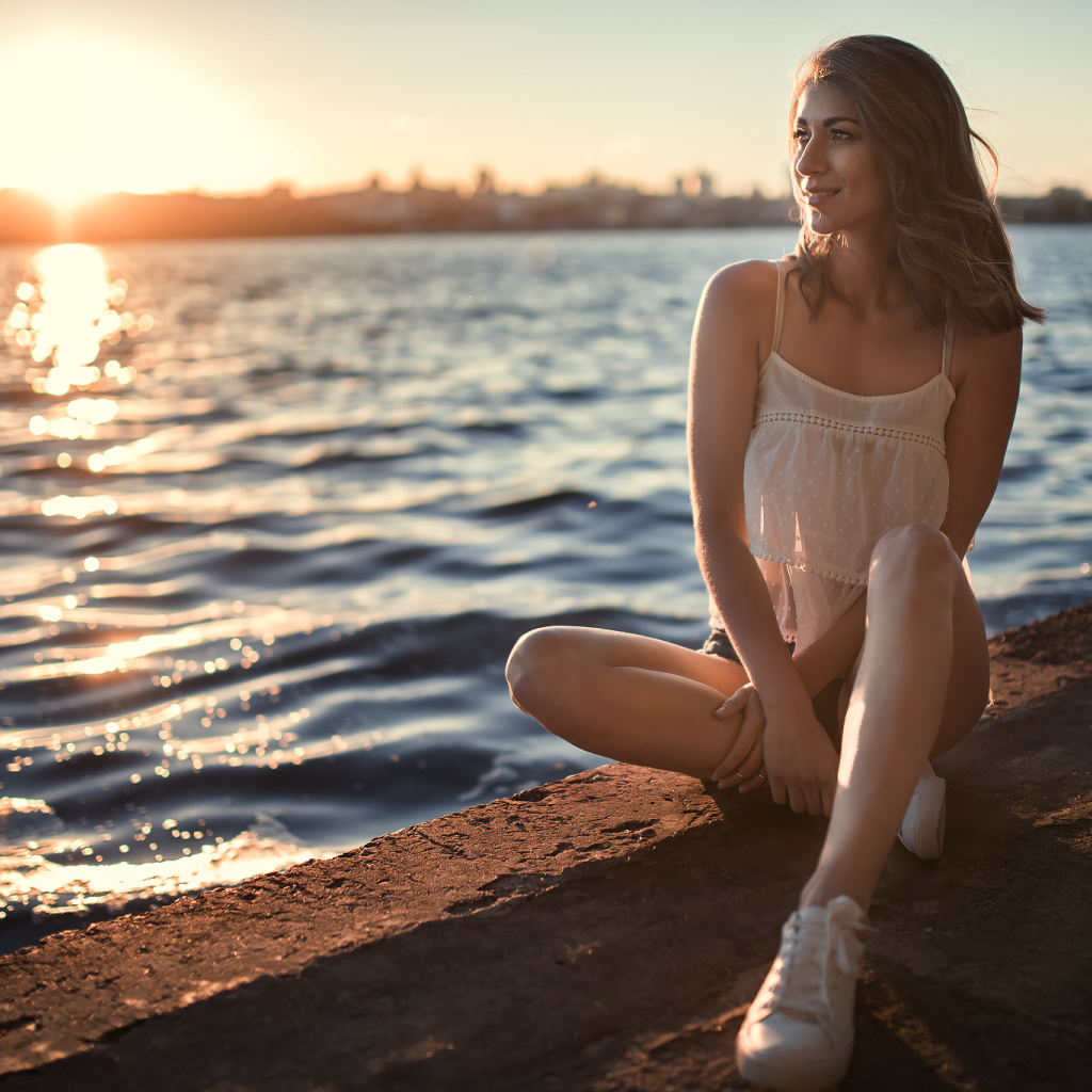 Красивая улыбающаяся девушка сидит в лучах солнца у реки