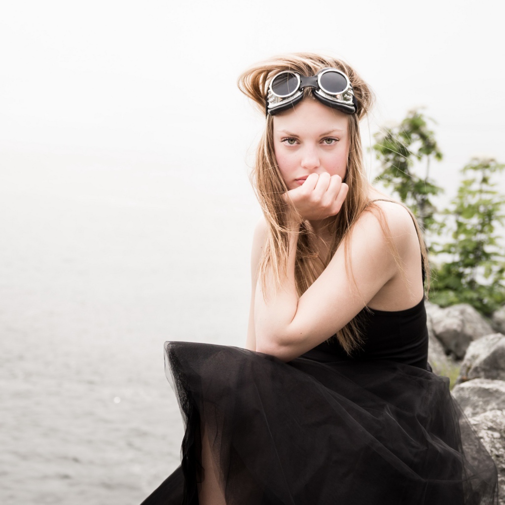 Девушка блондинка с очками на голове сидит на камне