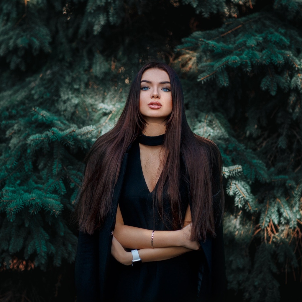 Голубоглазая девушка брюнетка у большой зеленой ели 