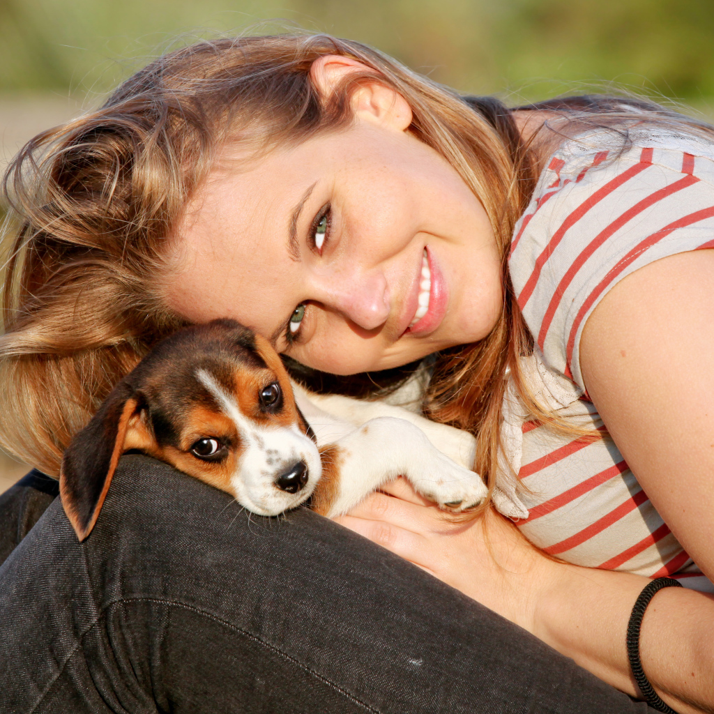 Убающаяся девушка шатенка с милым щенком на руках