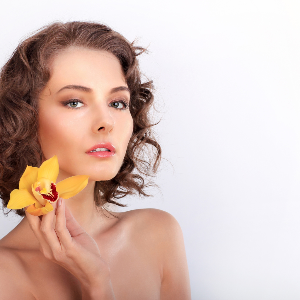 Нежная девушка шатенка с желтым цветком орхидеи в руке