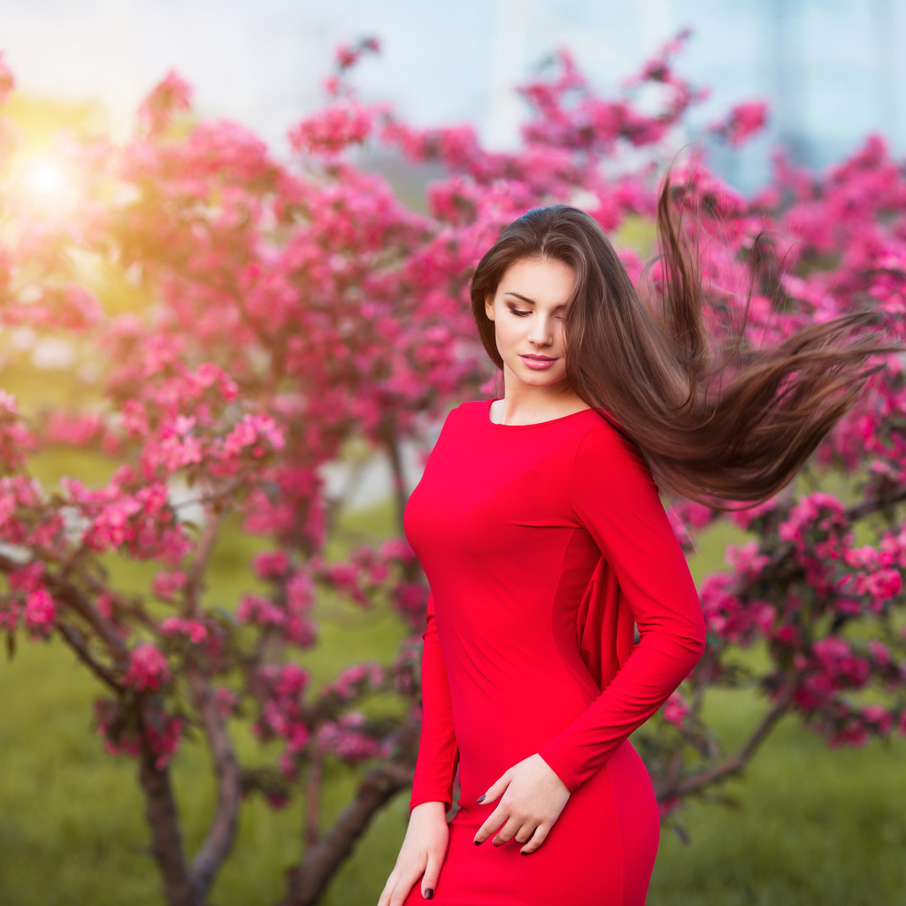 Милая шатенка в красном платье на фоне цветущего дерева