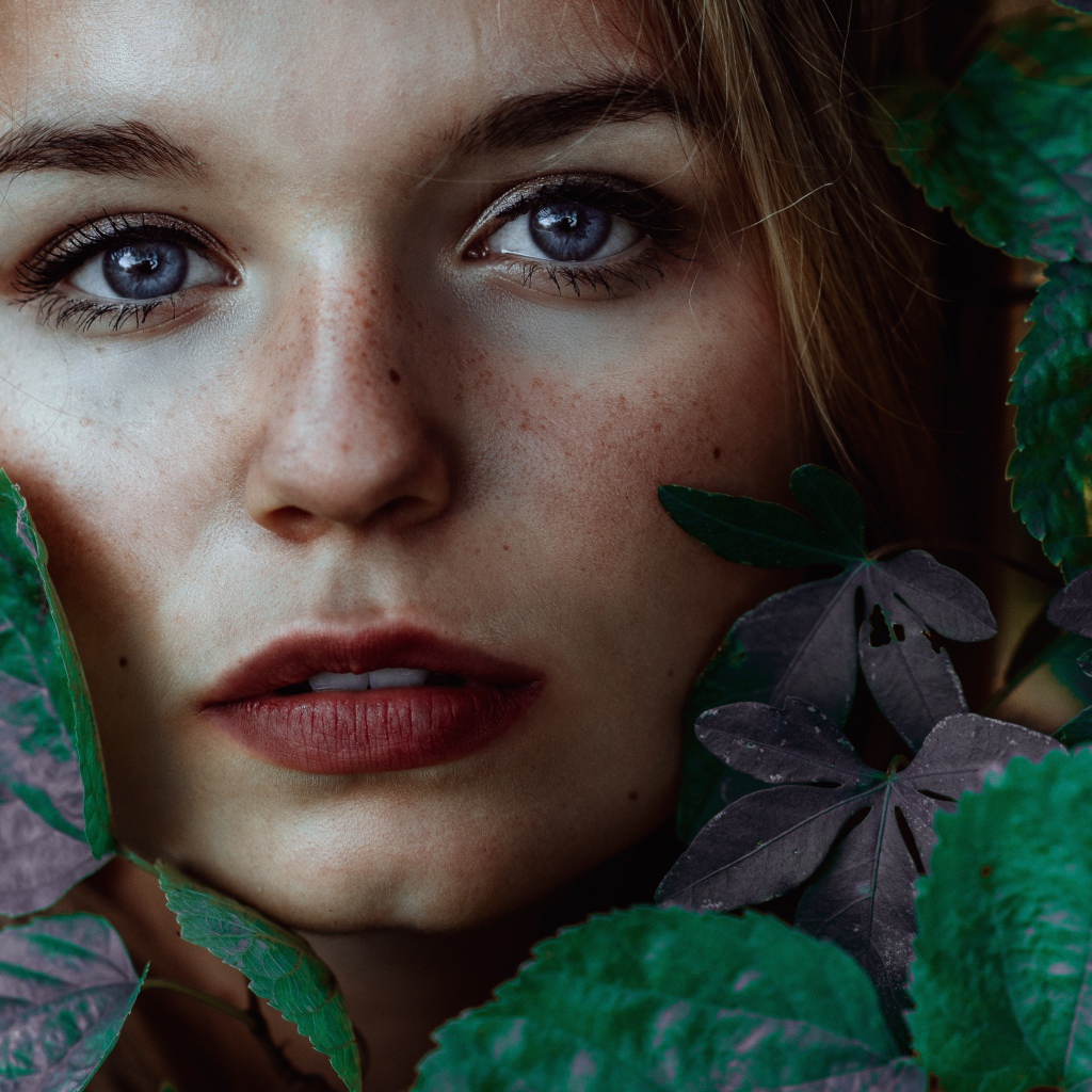 Лицо красивой голубоглазой девушки украшено зелеными листьями