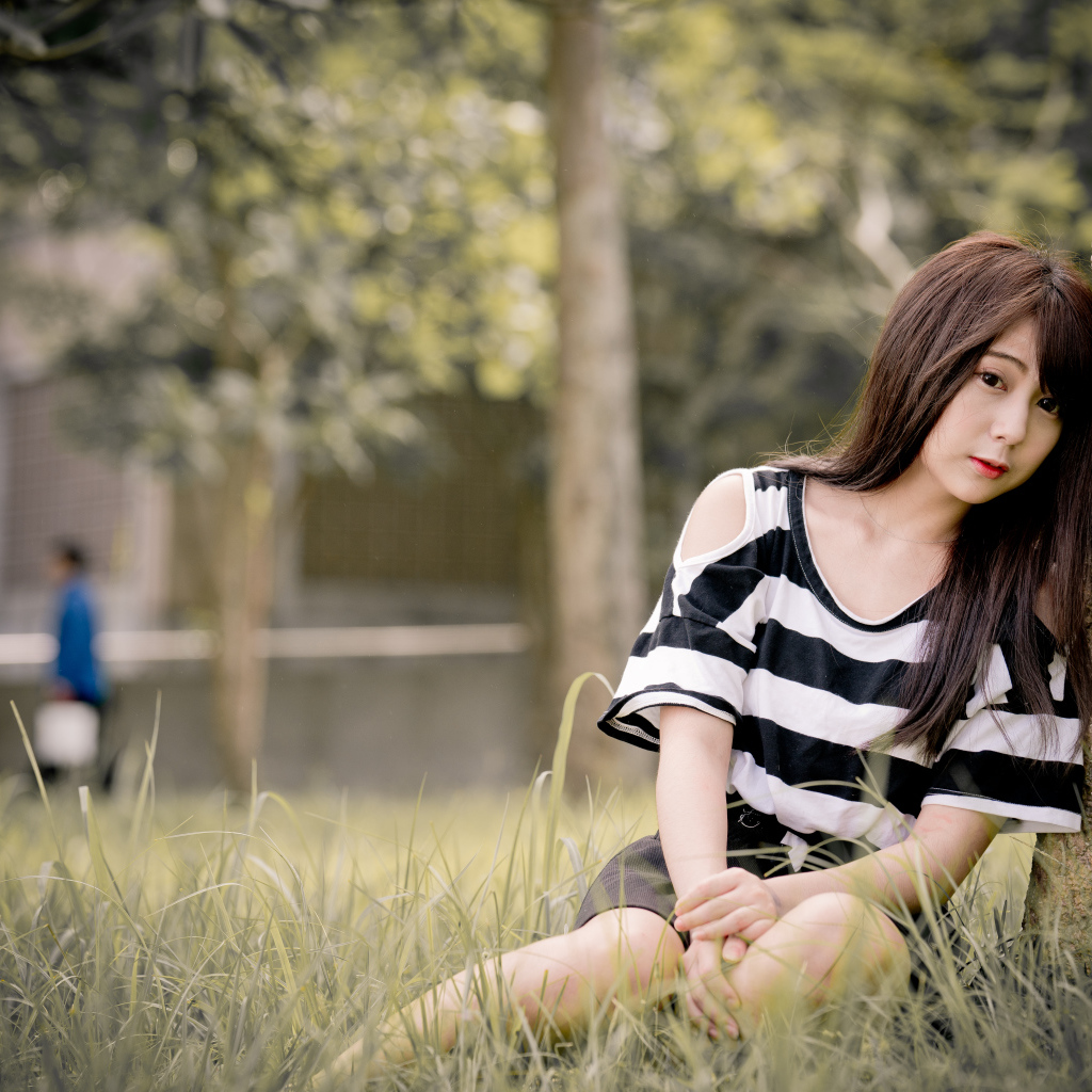 Молодая девушка азиатка сидит на траве у дерева