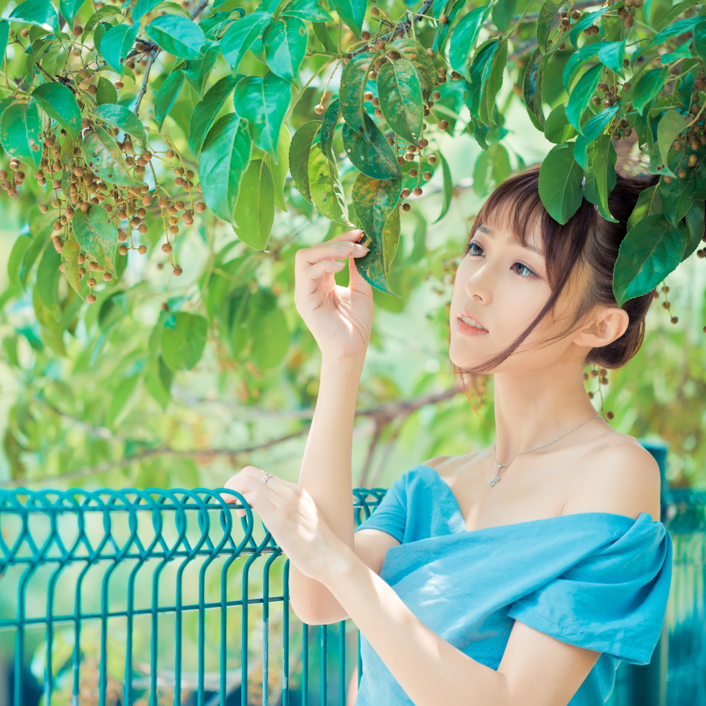 Молодая красивая девушка азиатка стоит у ветки с зелеными листьями