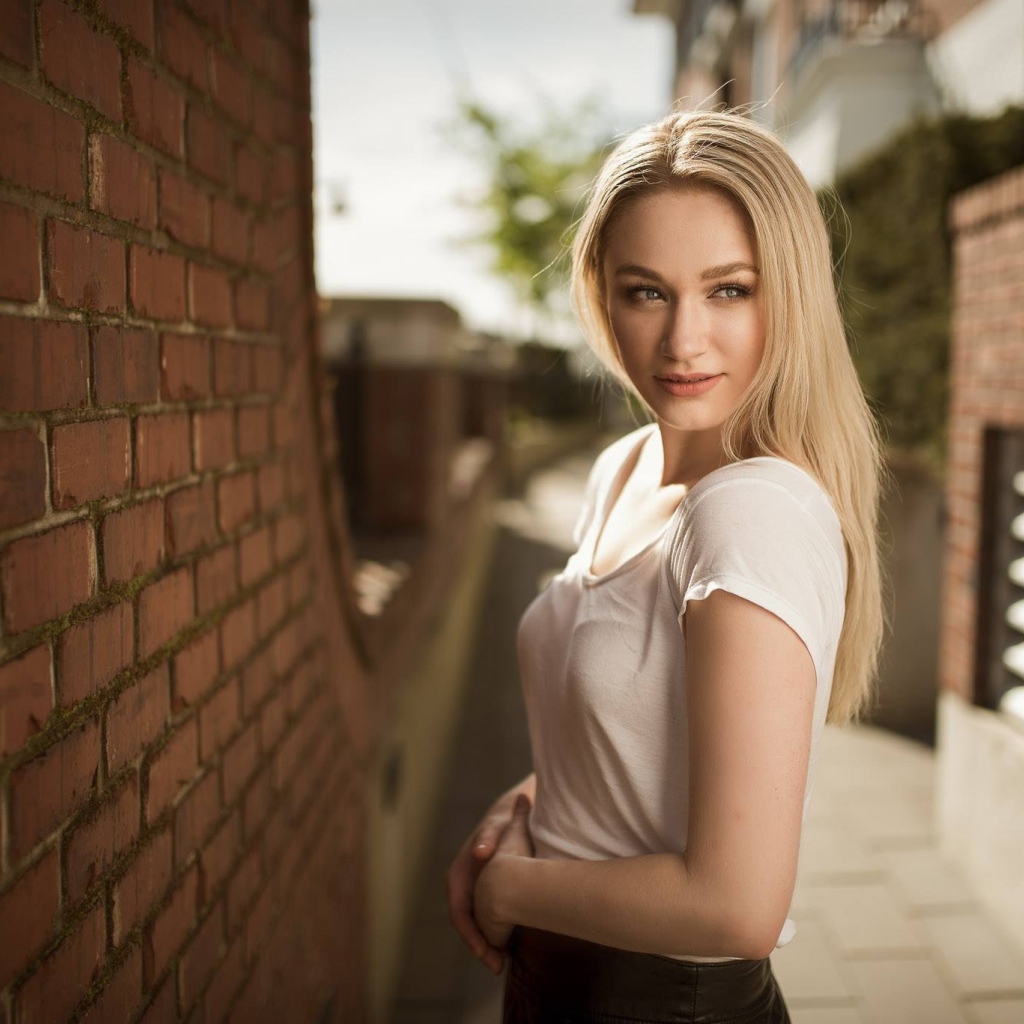 Молодая девушка блондинка у кирпичной стены 