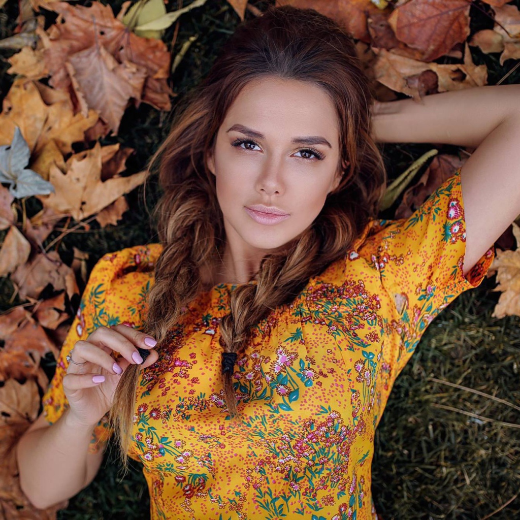 Молодая брюнетка лежит на траве с сухими листьями