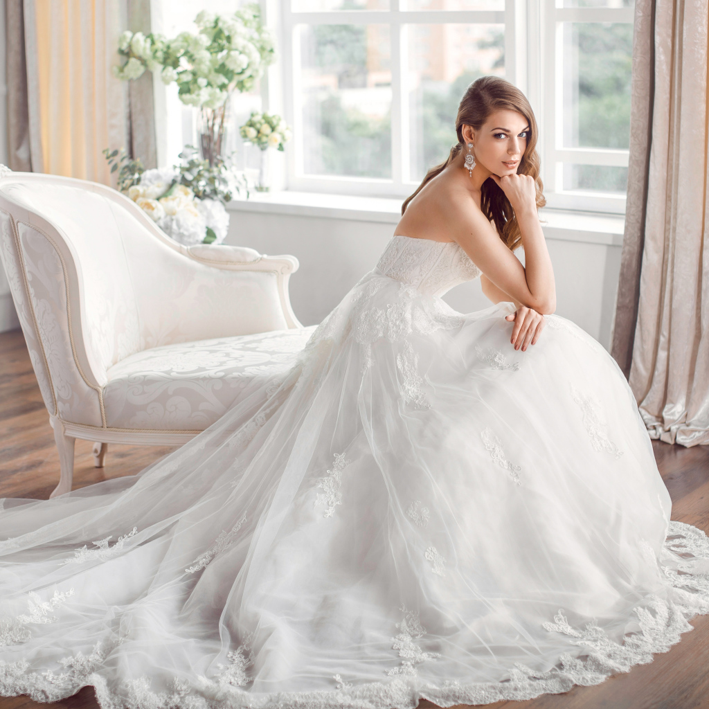 Молодая девушка в красивом свадебном платье сидит в белом кресле