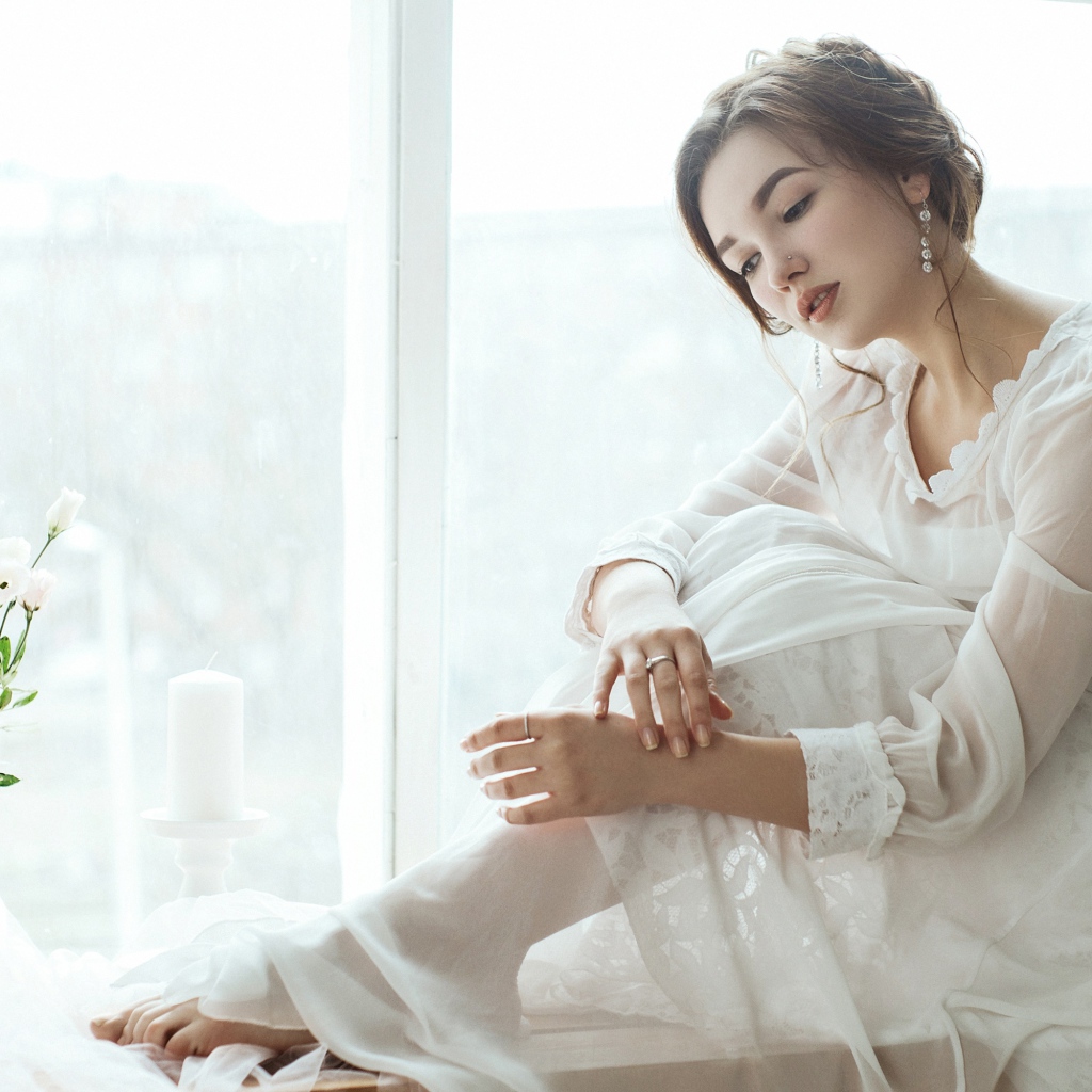 Молодая грустная девушка в белом платье у окна