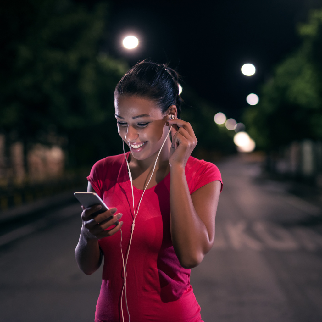 Молодая улыбающаяся девушка в наушниках с телефоном в руках