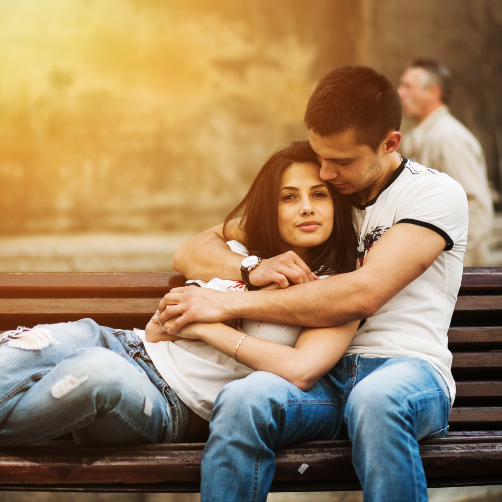 Влюбленная пара сидит на деревянной лавке в парке
