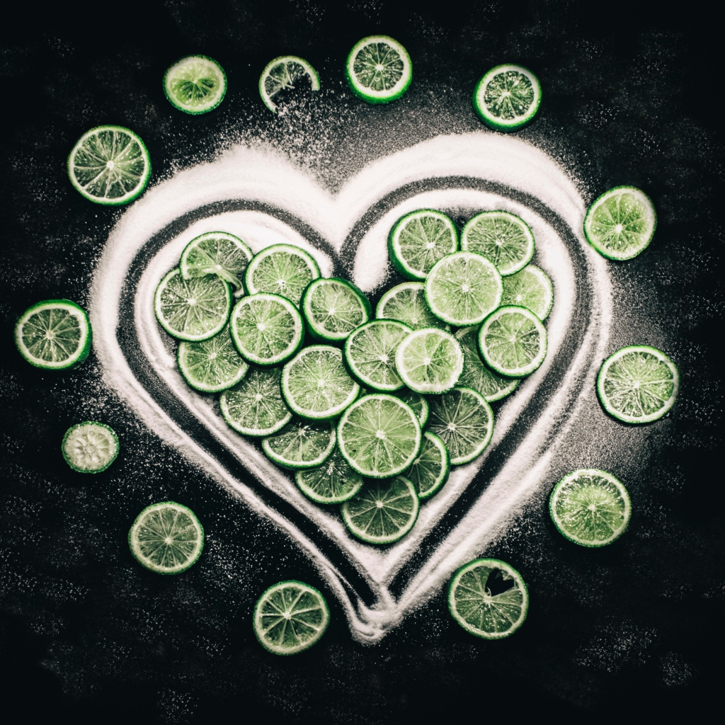 Сердце из сахара и кружочков  зеленого лайма на черном фоне