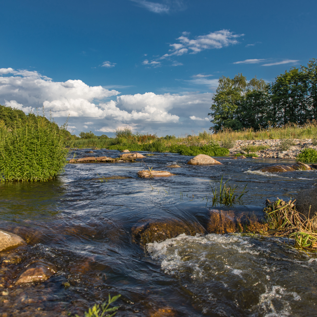 Быстрая речная вода стекает по камням под красивым голубым небом