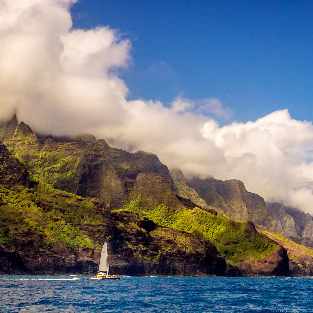 Парусная лодка плывет по голубой воде на фоне покрытых зеленью гор