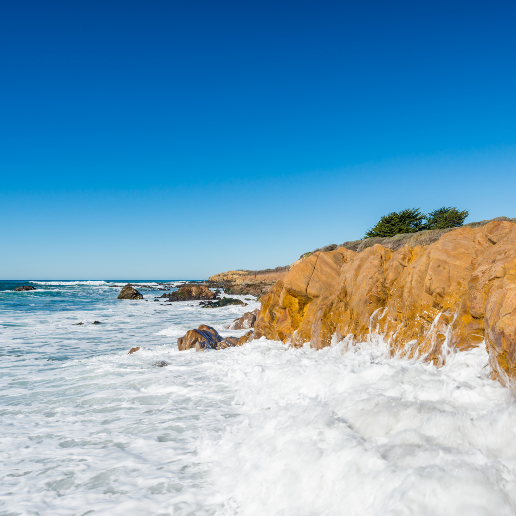 Белые волны бьются о скалы на берегу океана под голубым небом