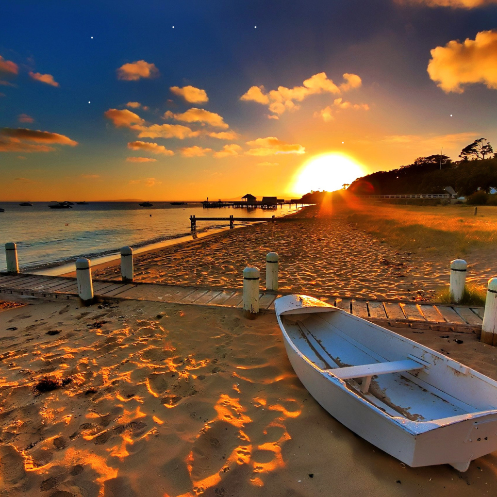 Белая лодка на пляже под закатным солнцем