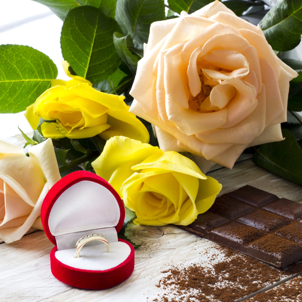 Букет роз на столе с шоколадкой и красной коробочкой с обручальным кольцом