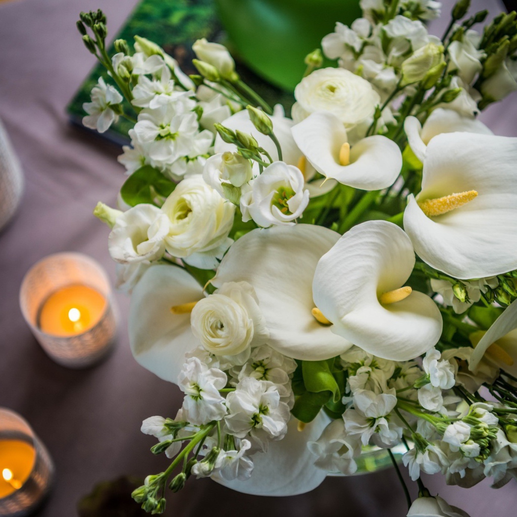 Букет белых цветов зантедеския и левкой с зажженными свечами на столе