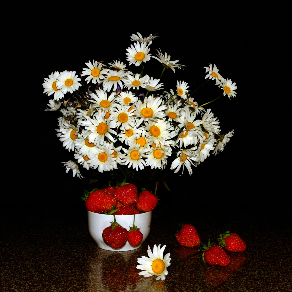 Белые полевые ромашки и клубника на столе на черном фоне