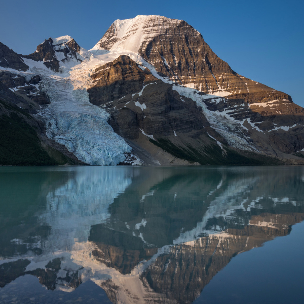 Гора в снегу отражается в водной глади озера 