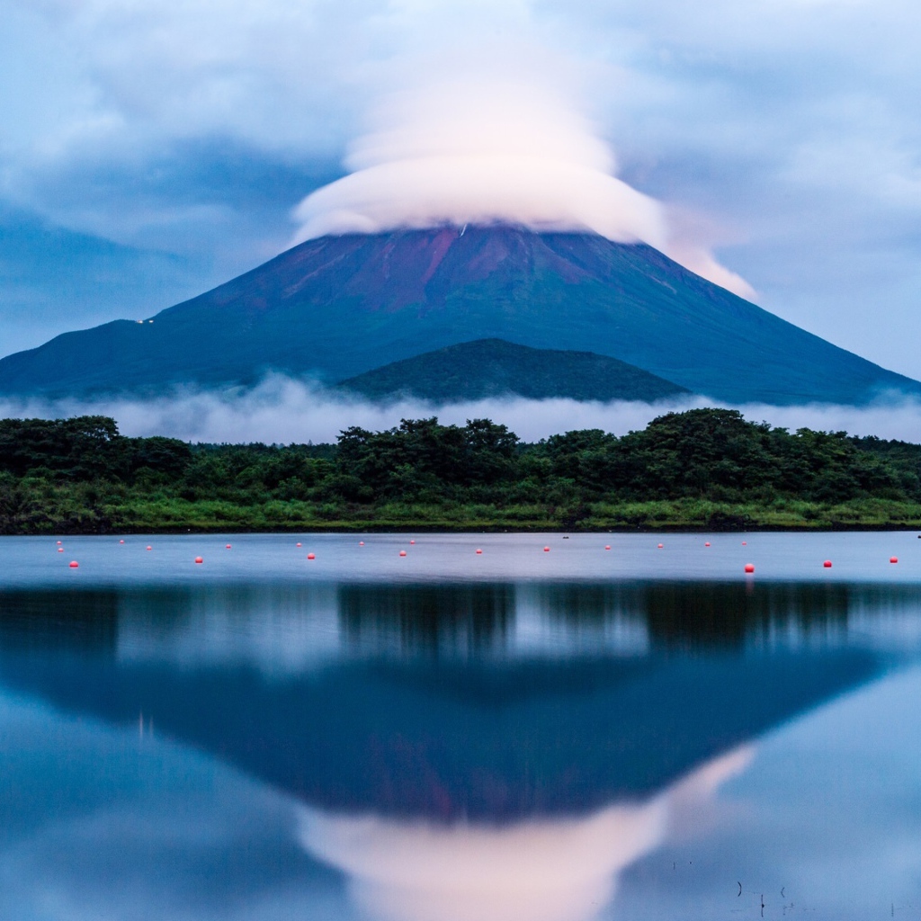 Вулкан Фудзияма в белых облаках отражается в воде озера