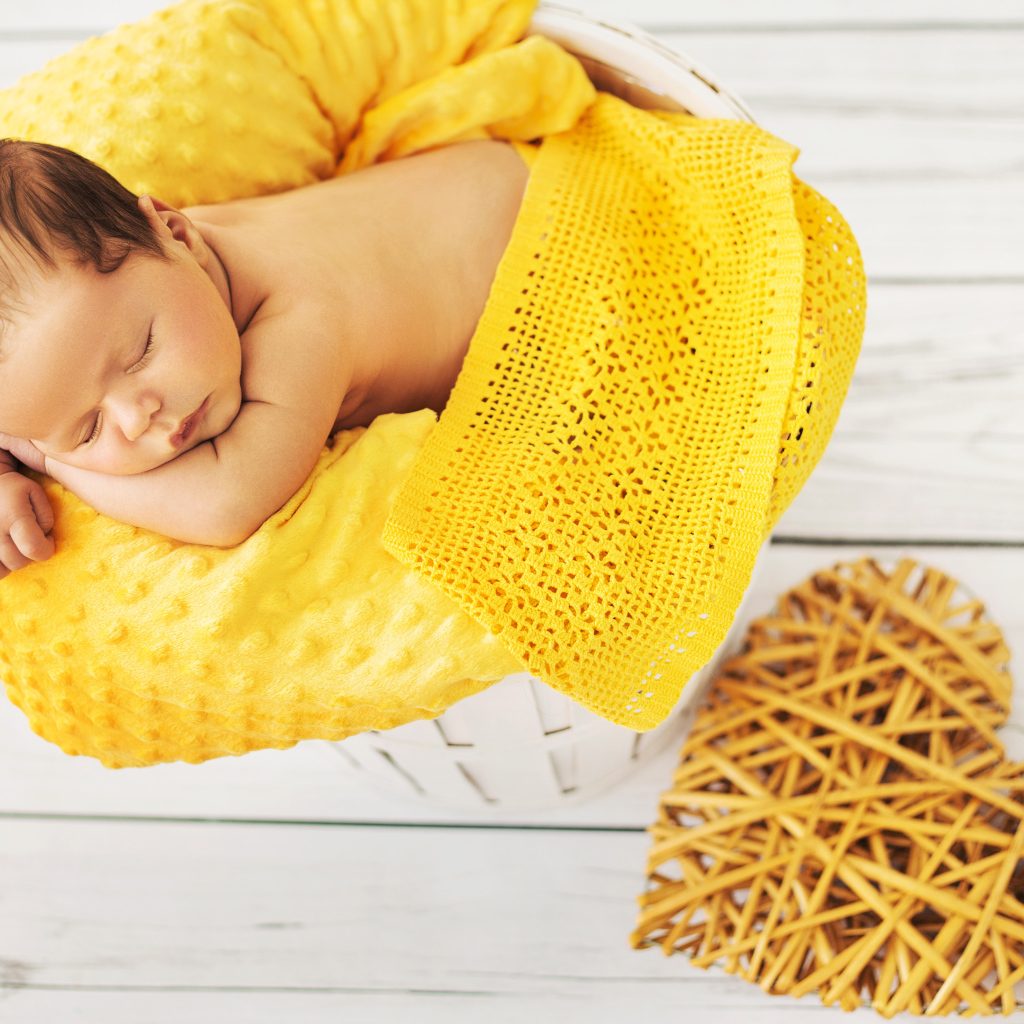 Грудной ребенок спит на желтой подушке с плетеным сердцем