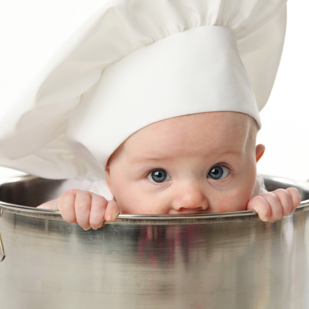 Грудной ребенок в шапке повара сидит в большой кастрюле