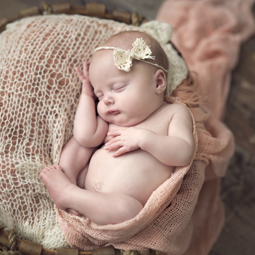 Грудной ребенок с бантиком на голове спит в корзине