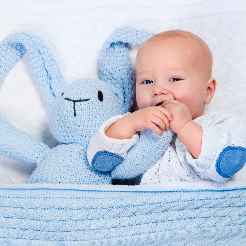 Милый младенец лежит в кроватке с голубым вязаным зайцем