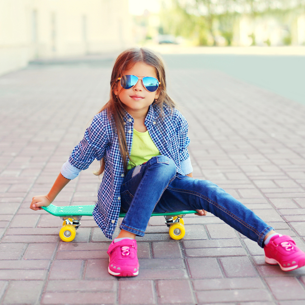 Девочка в солнечных очках сидит на скейтборде