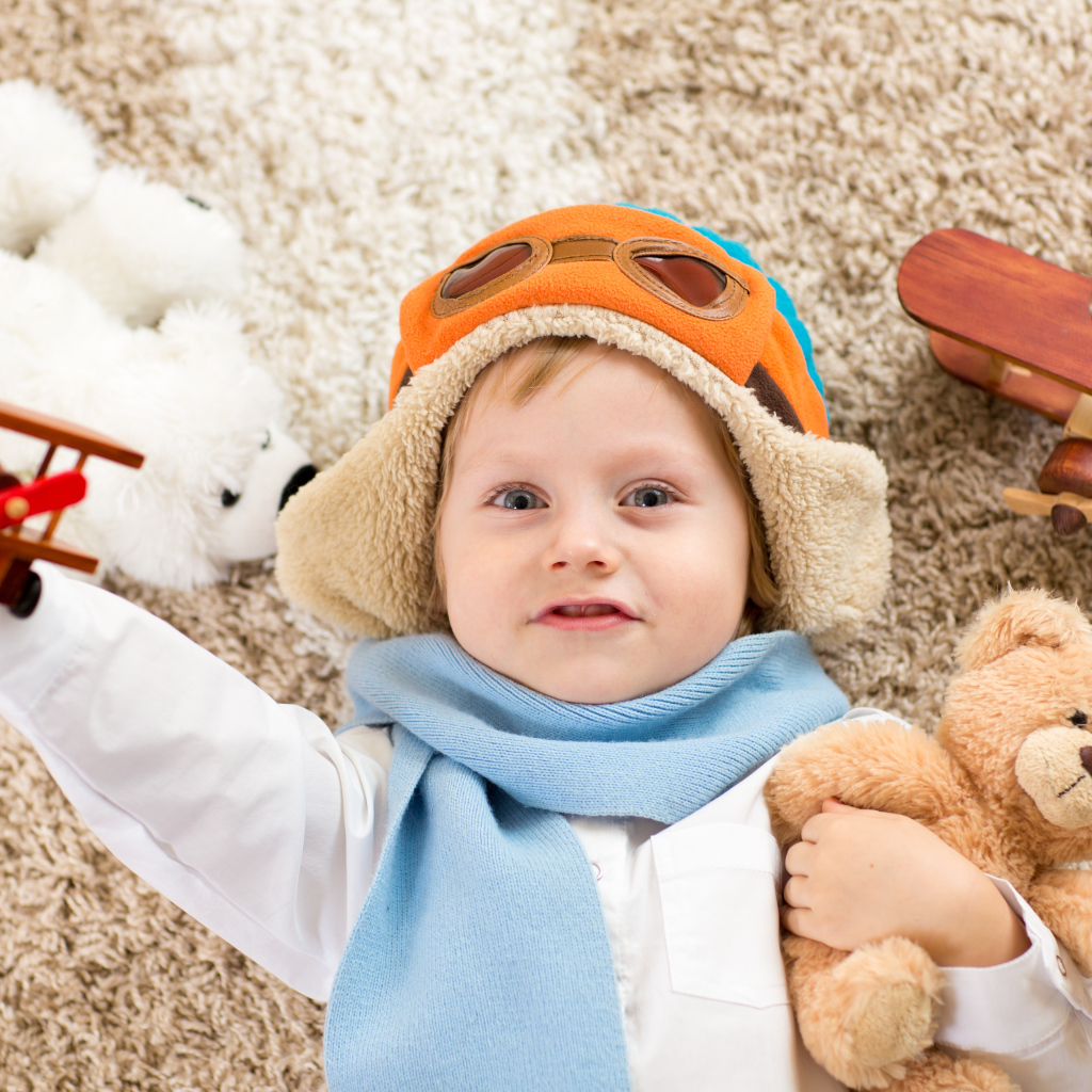 Маленький мальчик в шапке и игрушечным самолетом и медвежонком в руках