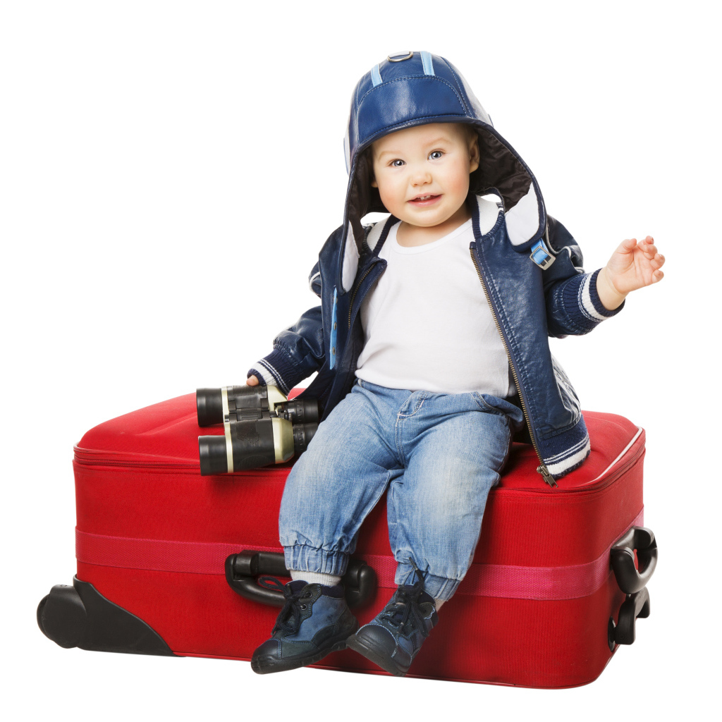 Маленький мальчик в шапке с биноклем сидит на красном чемодане