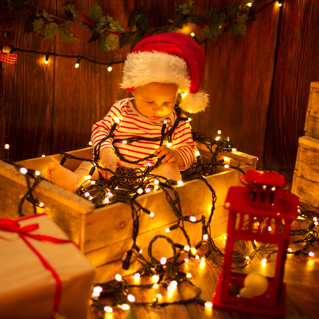 Маленький мальчик сидит в коробке с новогодней гирляндой