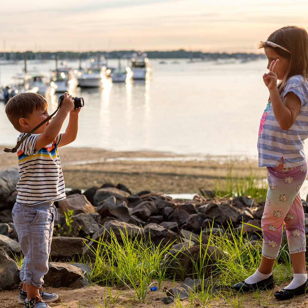 Маленький мальчик фотографирует девочку на берегу