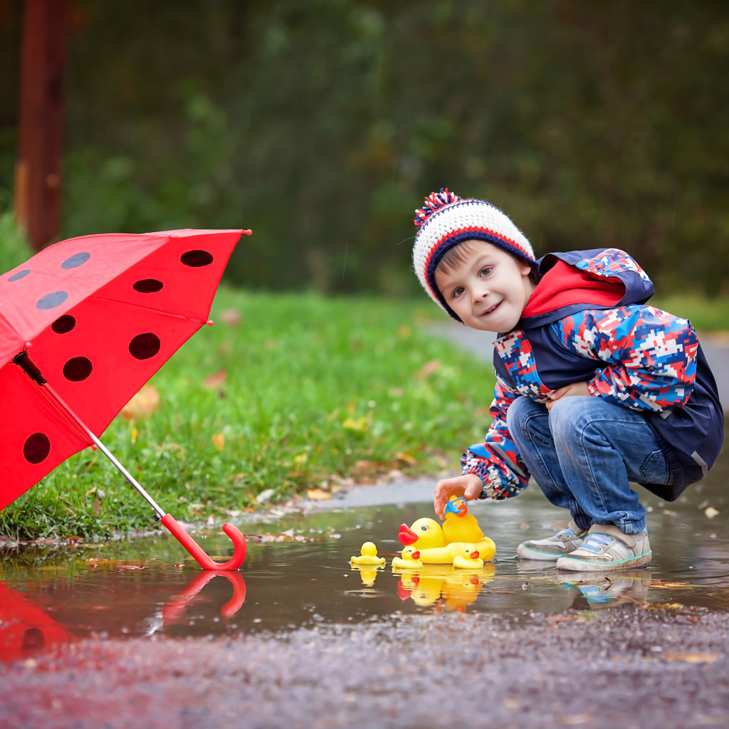 Маленький мальчик пускает резиновую уточку в лужу после дождя