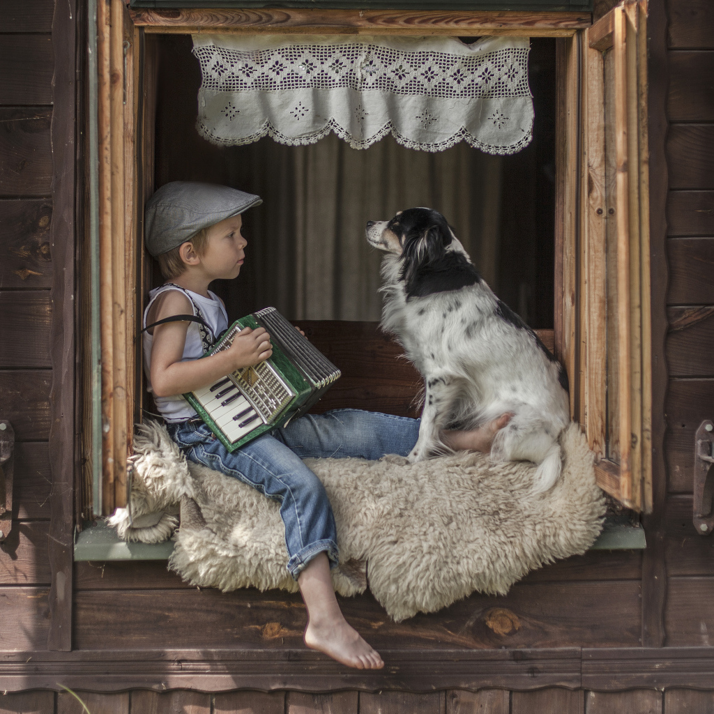Маленький мальчик с гармошкой сидит на подоконнике с собакой