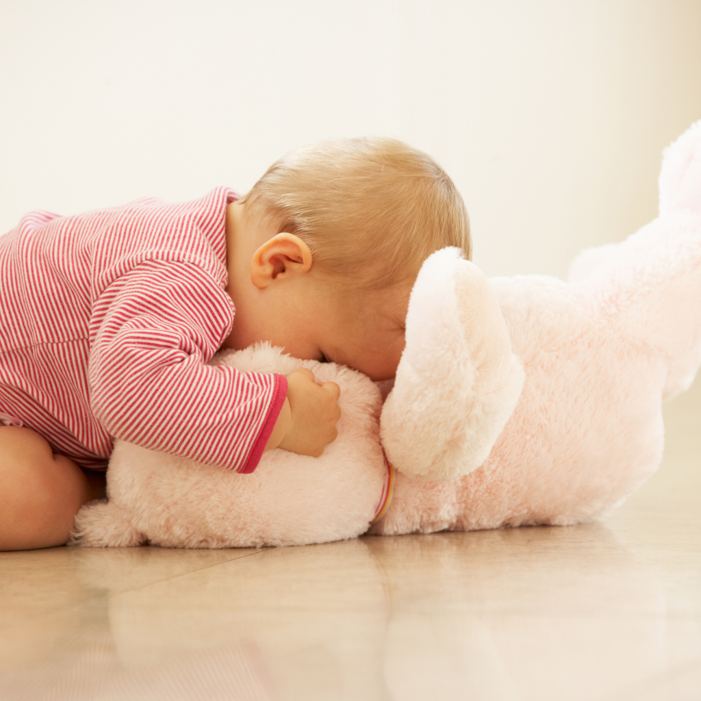 Маленький ребенок играет с розовым плюшевым мишкой