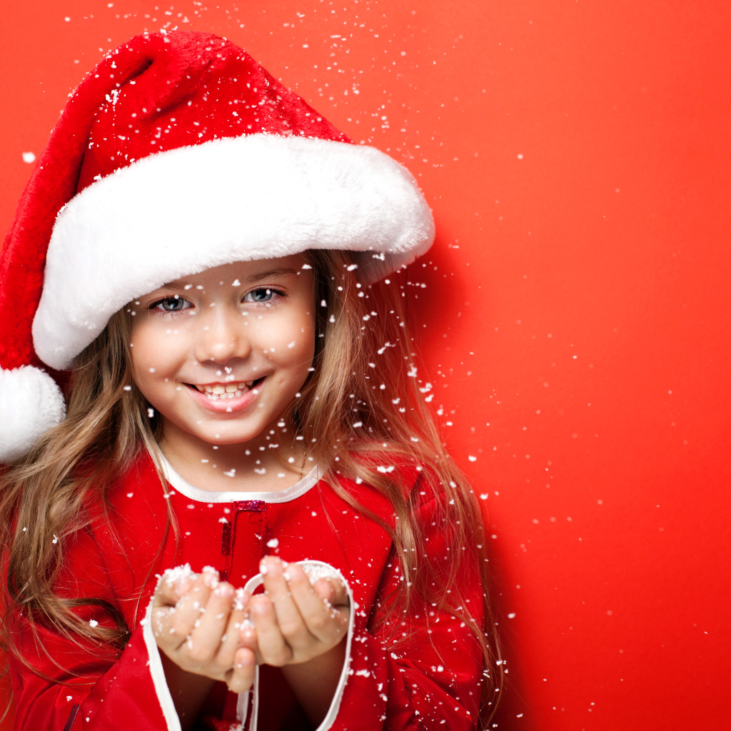 Маленькая девочка в новогодней шапке ловит руками снежинки