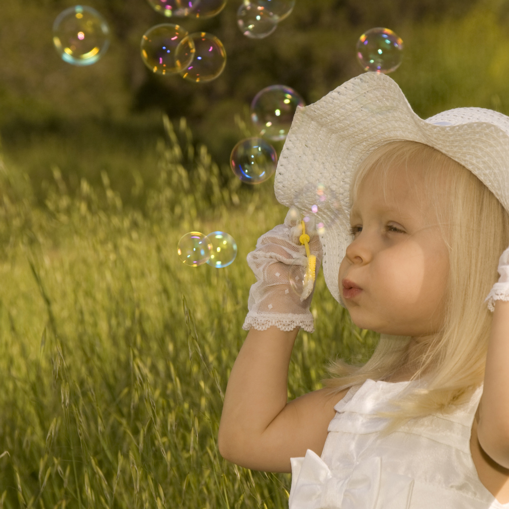 Маленькая девочка в большой белой шляпе пускает мыльные пузыри