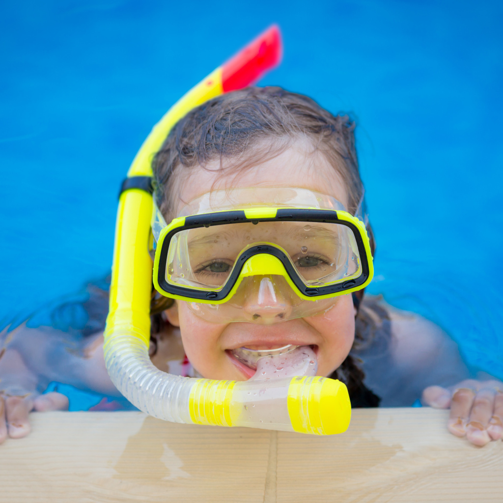 Маленькая девочка в маске с трубкой плавает в бассейне