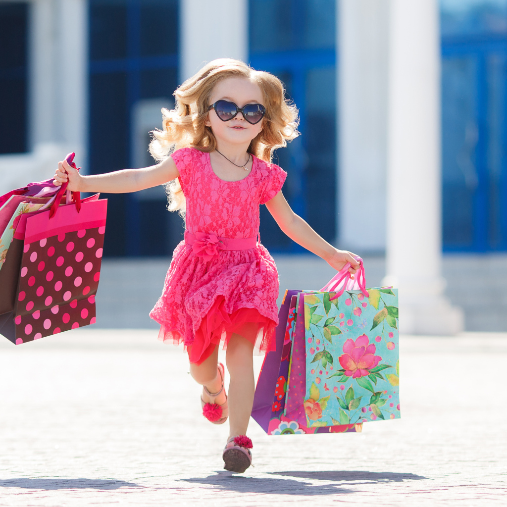 Маленькая девочка в розовом платье бежит с покупками из магазина