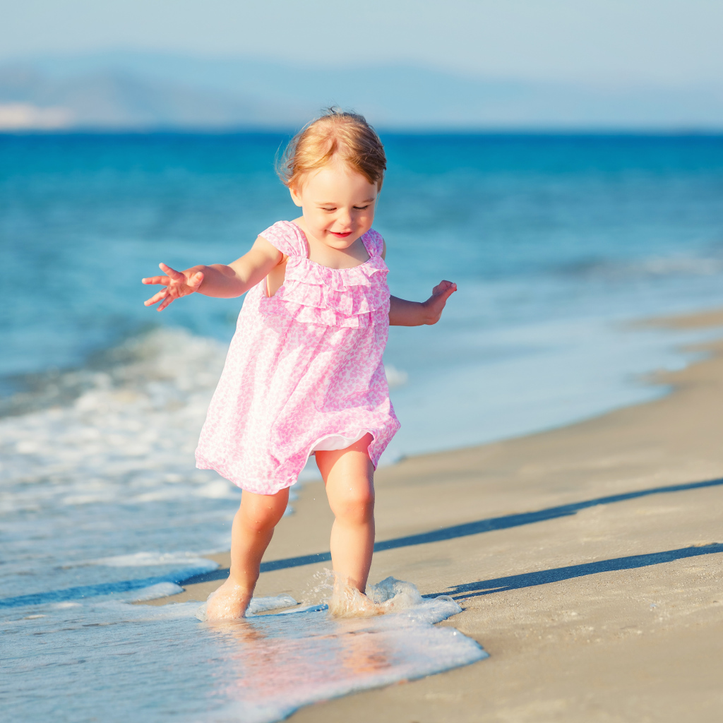 Маленькая девочка в розовом платье гуляет по морскому песку