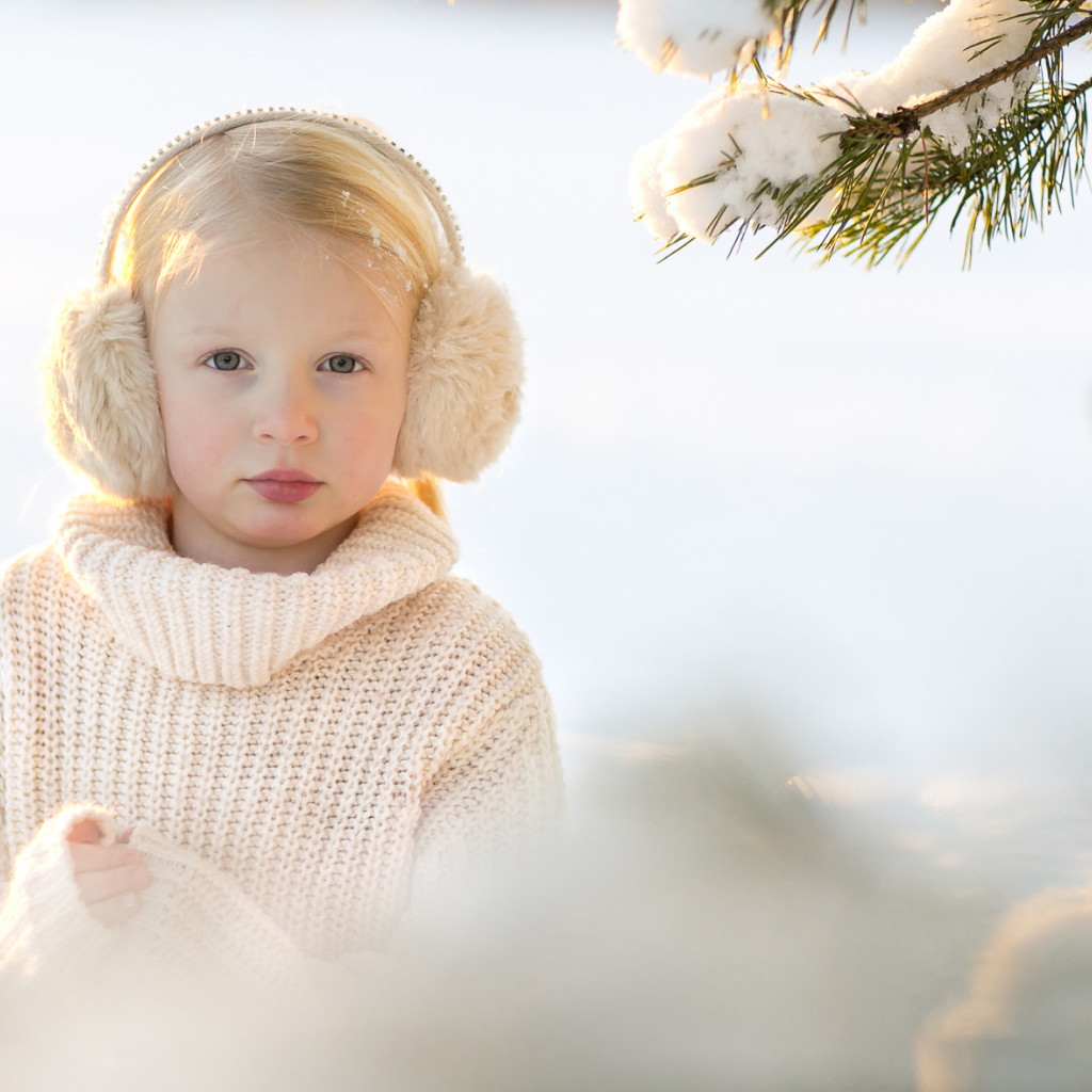 Маленькая девочка в белом свитере у покрытой снегом ели