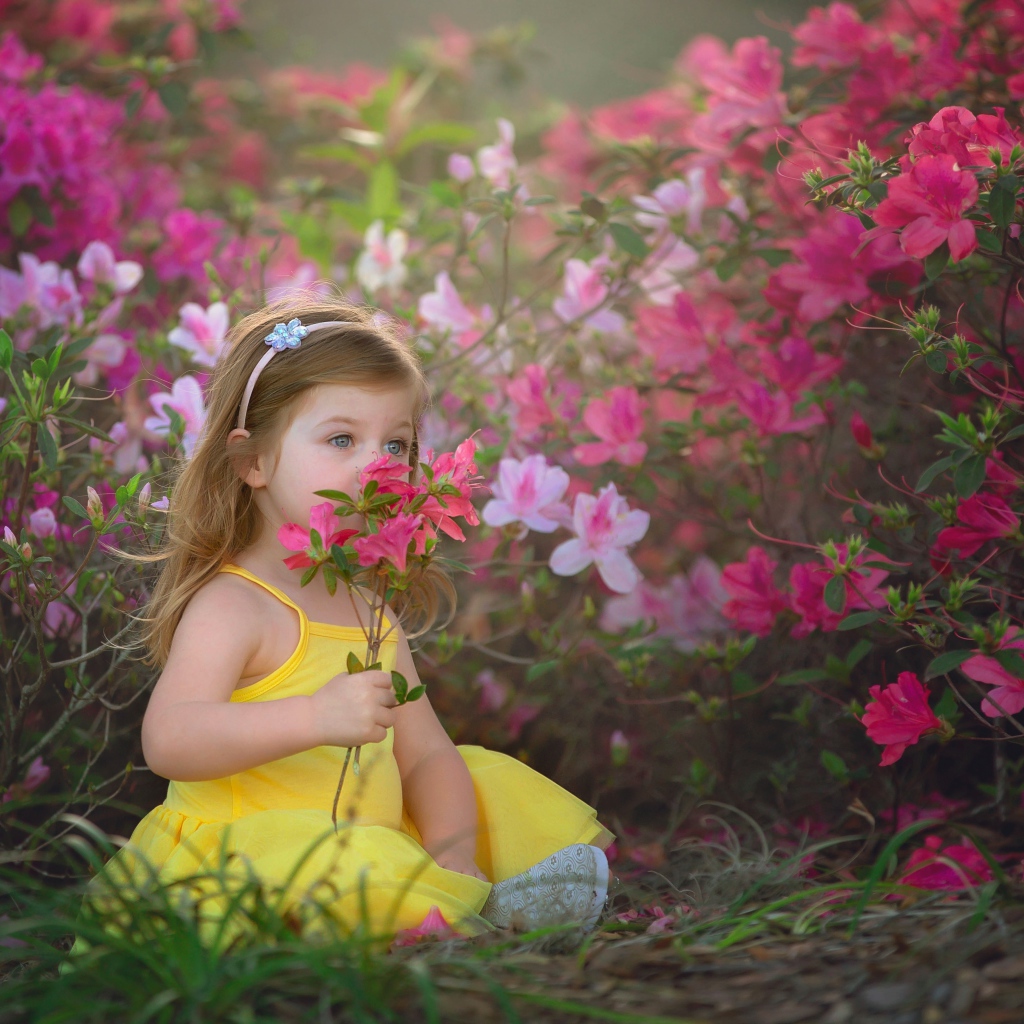 Маленькая девочка в желтом платье сидит рядом с розовыми цветами
