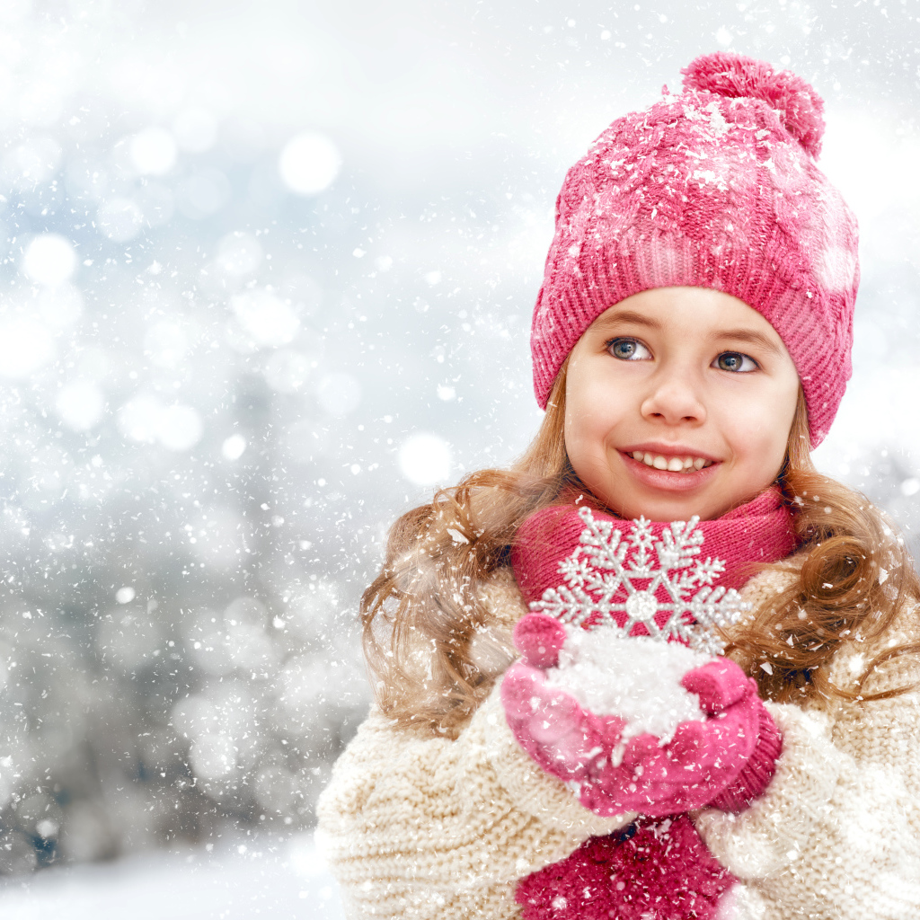 Маленькая девочка в зимней одежде держит снег в руках